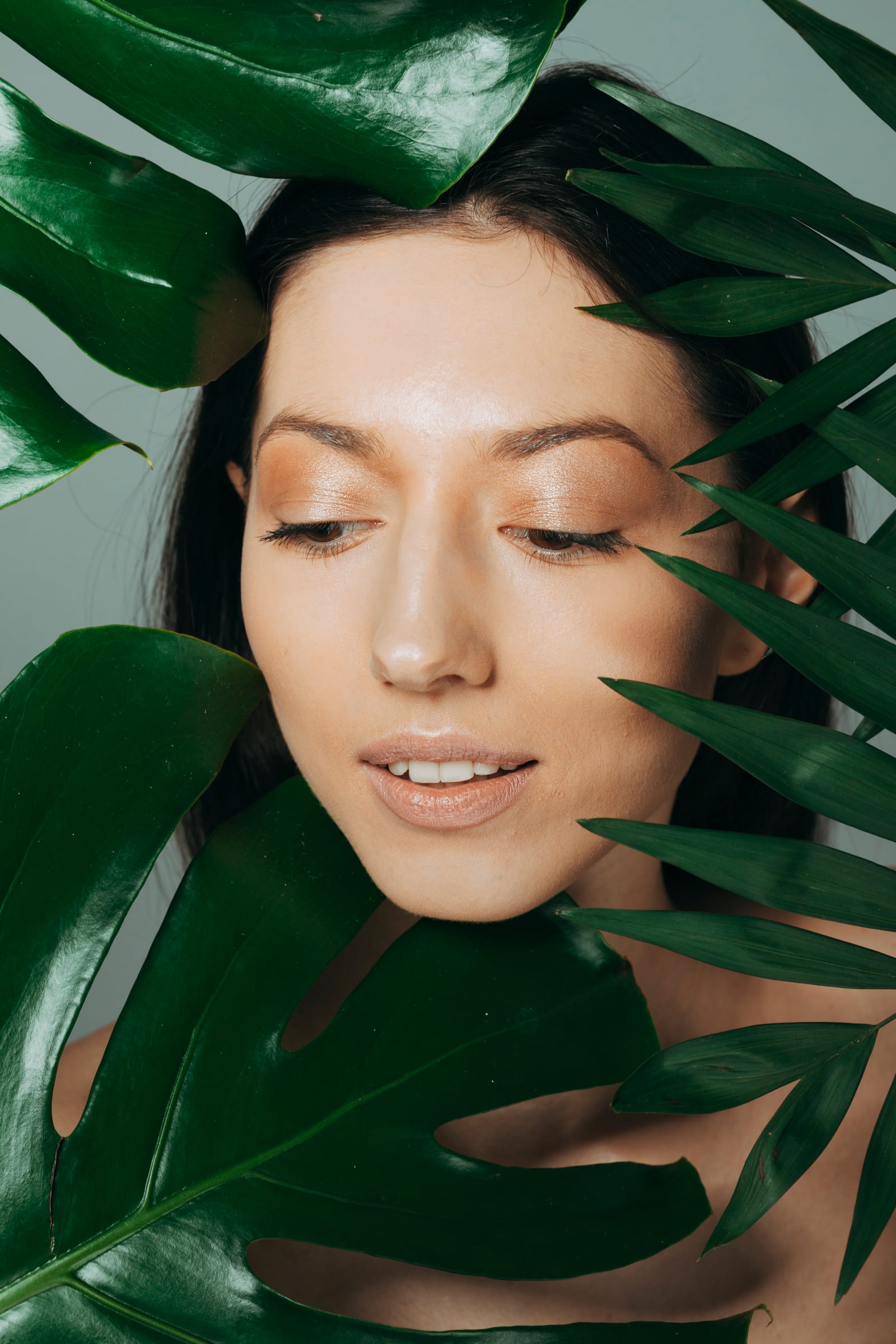 Rostro de mujer con piel luminosa entre hojas verdes de monstera y palmera